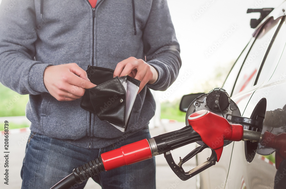 Lack of money for gasoline and fuel. Expensive gasoline. Driver man holds one dollar end empty wallet against the background of a fuel nozzle in the gas tank. increase in gasoline prices concept.